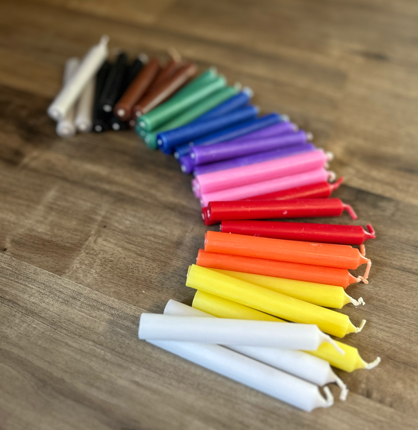 A colorful assortment of chime candles is arranged in rows. Each candle is tall and slender, with vibrant colors including red, orange, yellow, green, blue, and purple. The candles are displayed on a plain white background, highlighting their vivid hues and smooth, polished surfaces. Keywords: chime candles, colorful candles, candle assortment, vibrant colors, tall slender candles, red candle, orange candle, yellow candle, green candle, blue candle, purple candle